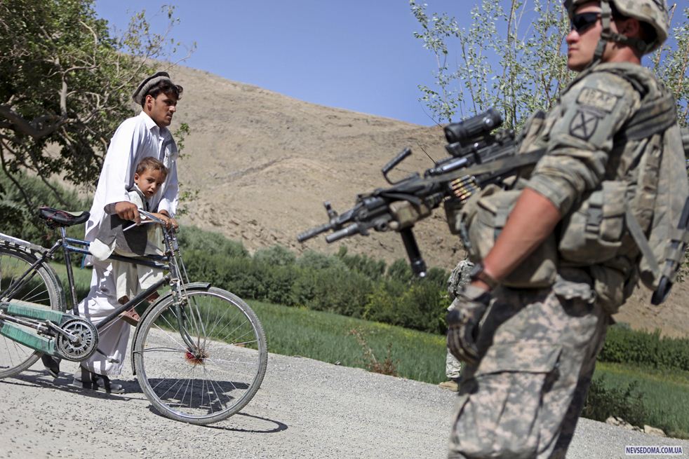 13. Мужчина с маленьким мальчиком проходят мимо рядового первого класса 22-летнего Майка Шмидта из Брунсвика, штат Мэн, во время его патрулирования в долине Танги в афганской провинции Вардак 16 августа 2009 года. (AP / David Goldman)